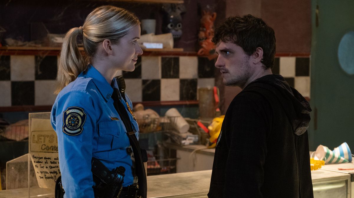 El guardia de seguridad nocturno Mike (Josh Hutcherson), magullado y con los ojos desorbitados, se enfrenta a la alegre policía Vanessa (Elizabeth Lali) en la película Five Nights at Freddy's.
