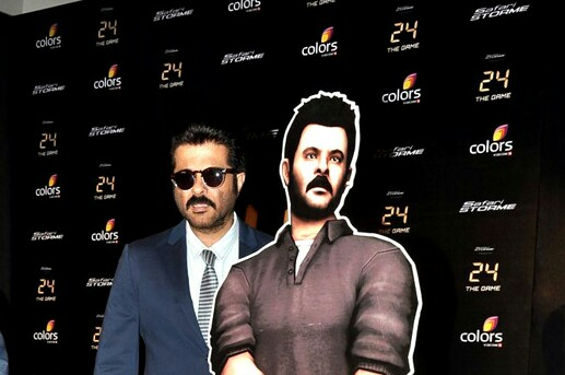 Anil Kapoor in a navy blue suit at the launch party of the "24" game with a cardboard cutout of his character in brown shirt. 