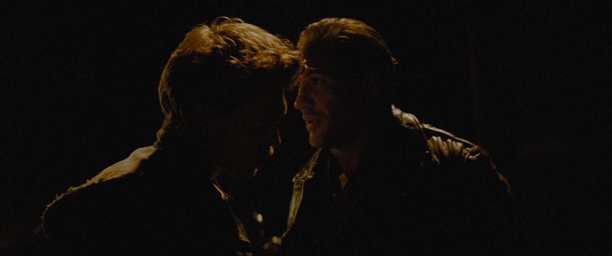 Austin Butler and Tom Hardy have an intense conversation, backlit and silhouetted in darkness in The Bikeriders