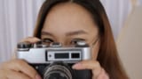 Egy női fotós szemüveges, kezében egy fényképezőgép