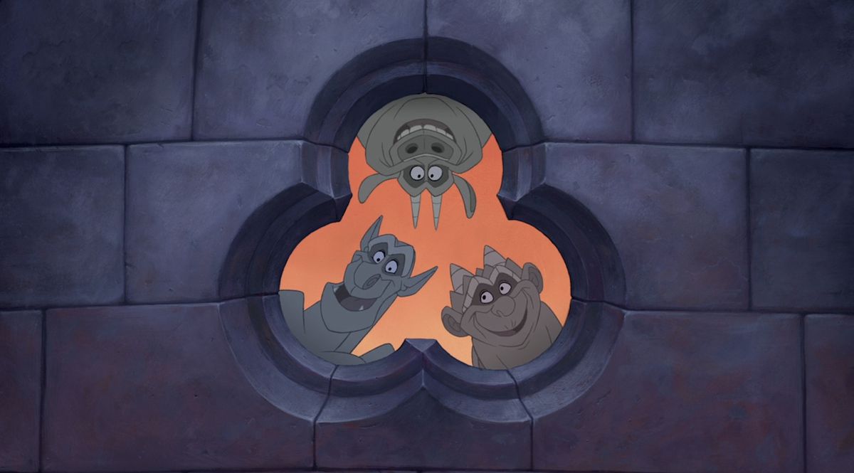 Victor, Hugo, and Laverne, the gargoyles from Disney’s 1996 animated movie The Hunchback of Notre Dame, all peer out of a trefoil-shaped window in a grey brick wall 