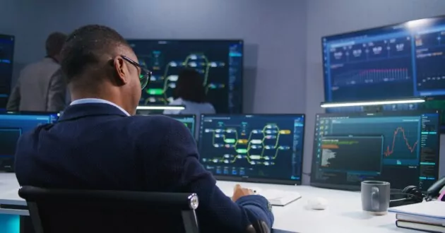 Software programmer sits in front of computer with blockchain network and data server in monitoring office. Team of IT technical specialists work with live analysis charts on big digital screens.