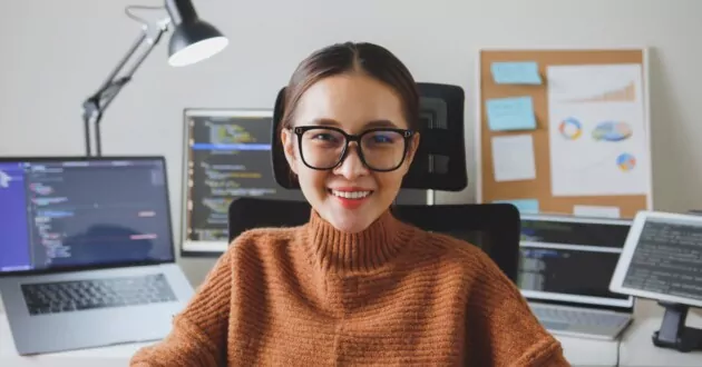 Portre genç geliştirici programcı, yazılım mühendisi, BT desteği, gözlük takan kameraya bakıyor ve gülümseyerek evde çalışmanın tadını çıkarıyor.