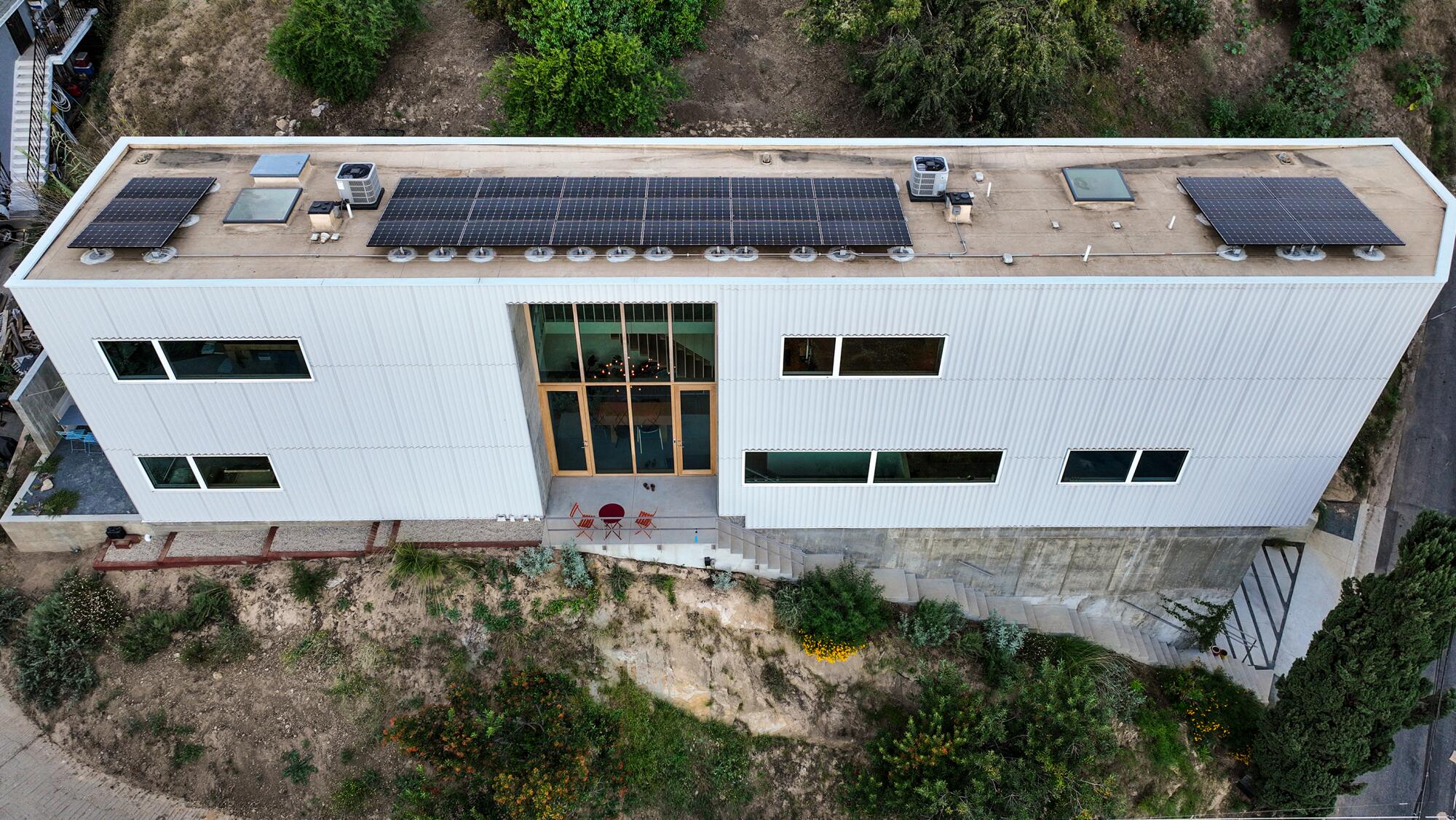 D’en haut, vous voyez la maison haute, mince et longue avec de grandes fenêtres verticales et des panneaux solaires sur le toit.