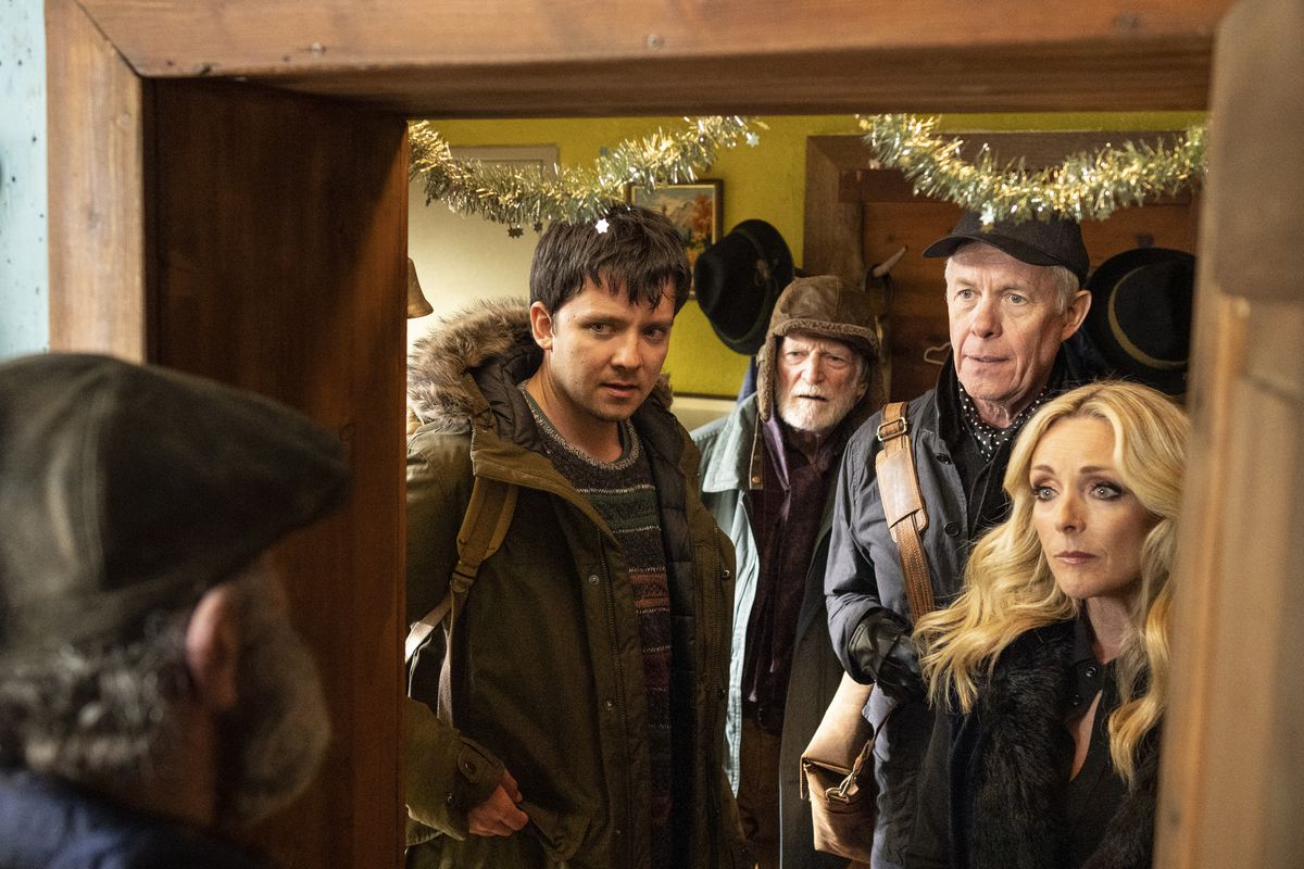 Asa Butterfield, two old men, and Jane Krakowski gather in the door frame of an old wooden ski lodge