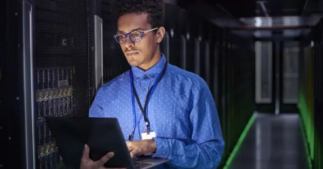 IT technician using laptop in dark server room