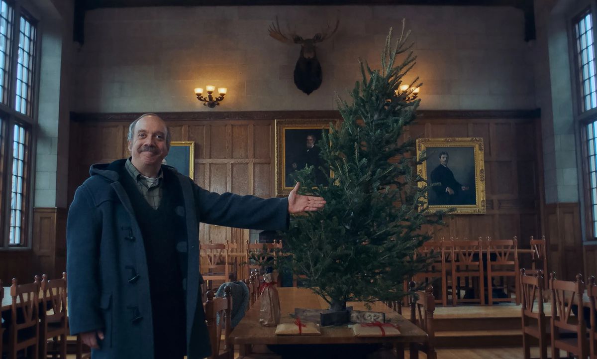 Paul Giamatti gesturing towards a tree in a large room in The Holdovers.