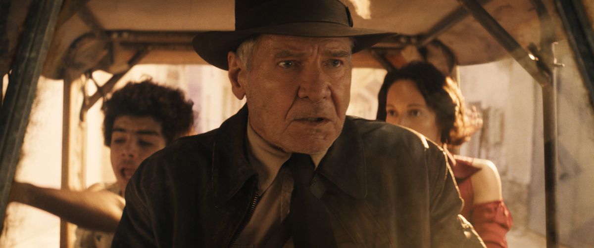 Indiana Jones parece entrar en pánico mientras conduce un carrito con Helena y Teddy en el asiento trasero en Indiana Jones y el dial del destino.