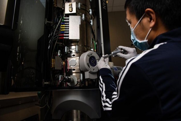 Wearing a mask and gloves, Yaobin Xu inserts a sample into a transmission electron microscope to examine the function of a rechargeable battery