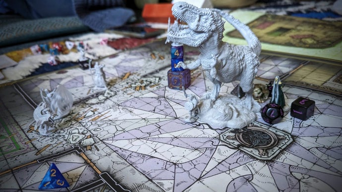Una fotografia di una grande mappa del pavimento di Dungeons & Dragons in formato poster con varie miniature posizionate sopra. Ci sono alcuni umanoidi fantasy in giro, ma il fulcro innegabile della scena è un gigantesco T rex. Quello è Bertie, cioè, trasformato per l'occasione. Lo ha tenuto in lotta.