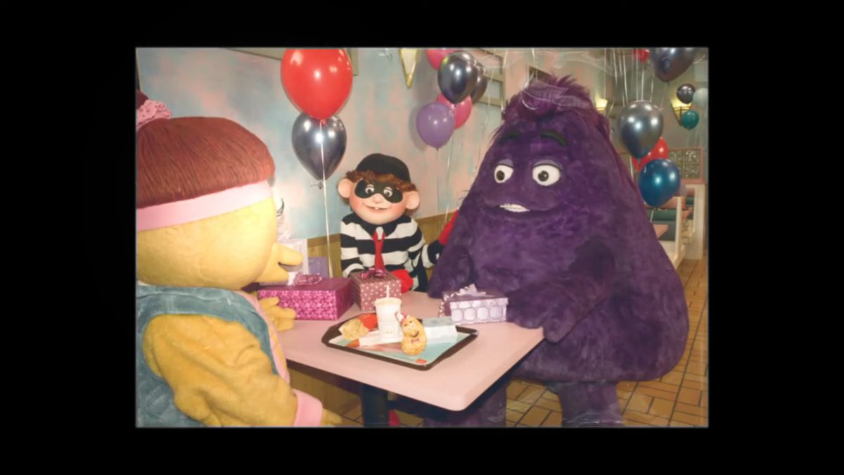 O fotografie veche cu Grimace, Hamburgler și un Birdie și Early Bird stând în jurul unei mese, mâncând McDonald’s.