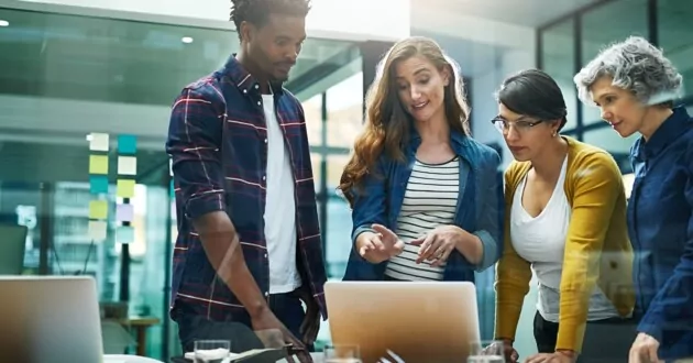 На снимке группа творческих бизнесменов, проводящих мозговой штурм по внедрению Oracle, стоя возле ноутбука в офисе.