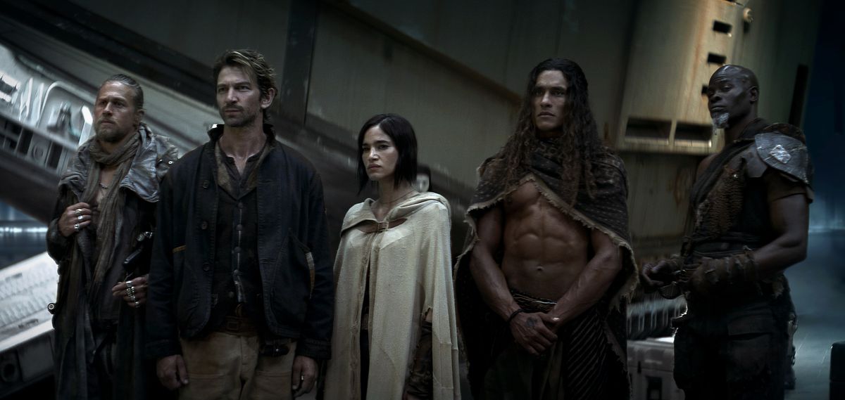 A group shot from Rebel Moon Part One: A Child of Fire, looking a little like a Dune cosplay group, with everyone in grubby, battered, earth-toned retro-futuristic robes or armor. Charlie Hunnam as Kai, Michiel Huisman as Gunnar, Sofia Boutella as Kora, Staz Nair as Tarak, and Djimon Hounsou as Titus.