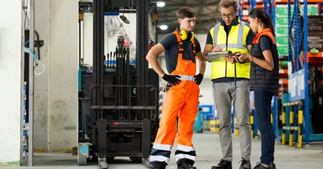 Trije inženirji se med seboj pogovarjajo v tovarni in gledajo iPad