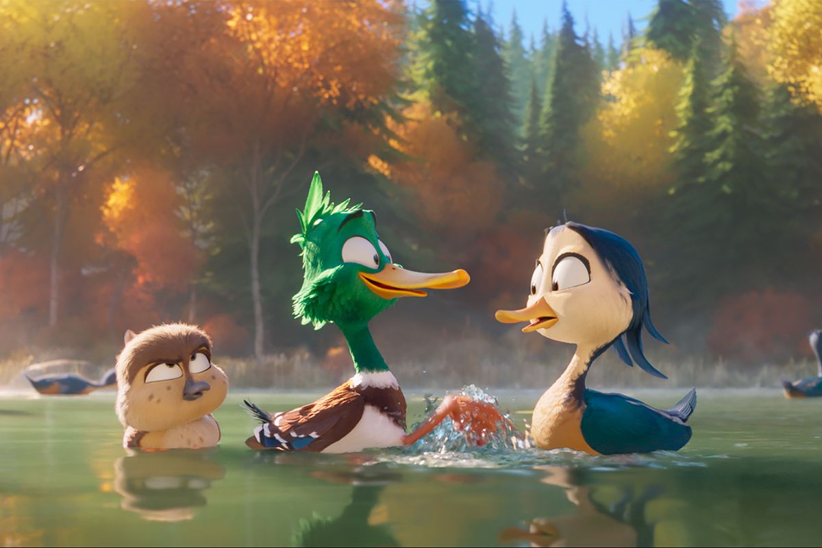 Um filhote de pato-real, um pato-real pré-adolescente com penas verdes e uma garça-real azul espirrando em um lago ao lado de árvores de outono em Migração.