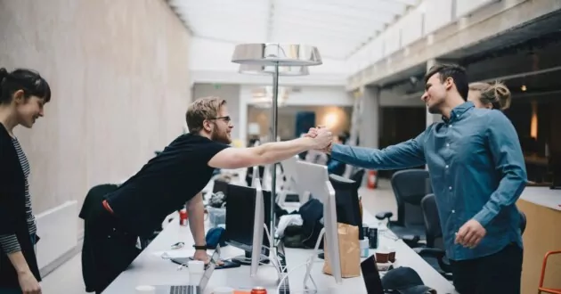 Programatori de computere bărbați ținând mâinile peste birou în birou, sărbătorind un pas de succes al strategiei de transformare digitală