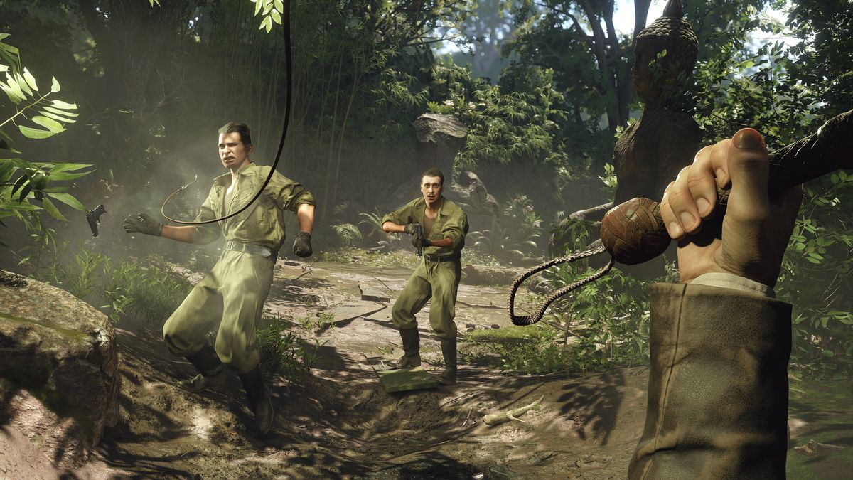 Eine Ego-Perspektive aus der Perspektive von Indiana Jones, mit erhobener Peitsche, um zwei Nazi-Soldaten in einer Dschungelkulisse aus dem Spiel „Indiana Jones and the Great Circle“ zu schlagen