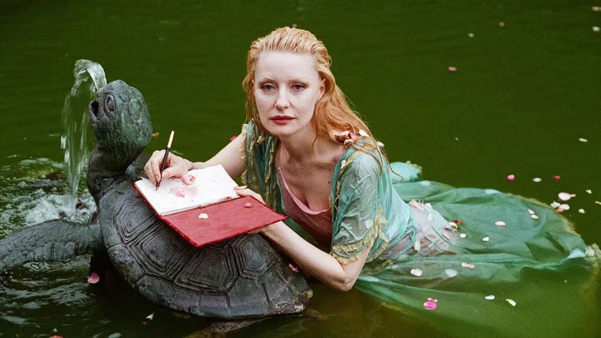 Foto Shere Hite som ligger i en vannbasseng og skriver i en rød journal på toppen av en steinskilpaddefontene i dokumentaren «The Disappearance of Shere Hite». 