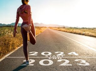Un corredor se estira ante una línea de salida que dice "fin de 2023" y "inicio de 2024"
