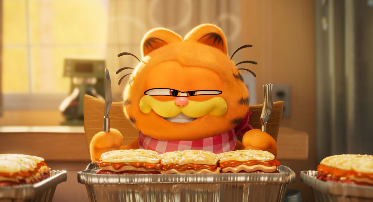 Een geanimeerde Garfield, die een slabbetje draagt ​​en een vork en een mes vasthoudt, is klaar om absoluut wat lasagne te eten in The Garfield Movie.