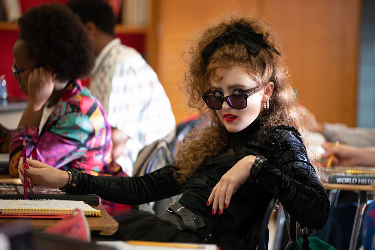 Kathryn Newton, med stort hår, sidder ved en skolepult i Lisa Frankenstein