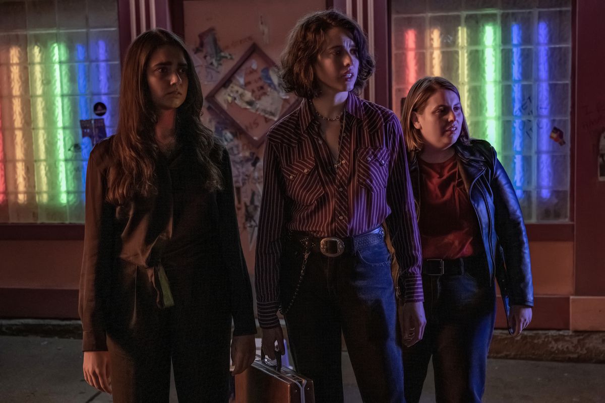Geraldine Viswanathan, Margaret Qualley, and Beanie Feldstein stand outside of what looks like a bar in Drive-Away Dolls