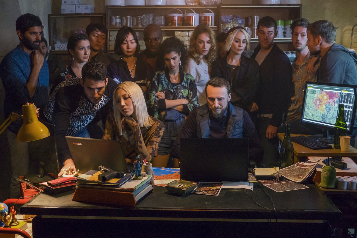 Un grup de oameni, inclusiv distribuția principală din Sense8, stând peste umărul a două persoane care tastează pe laptopuri în Sense8.