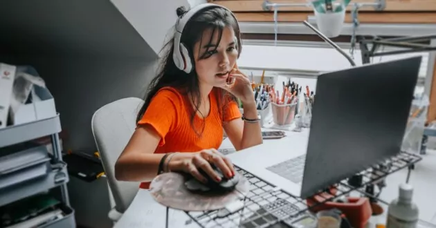 Junger Mensch singt mit Kopfhörern, während er zu Hause am Laptop arbeitet